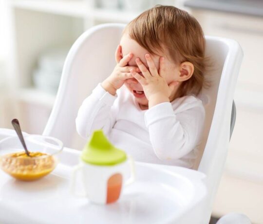 παιδάκι σε καρεκλάκι φαγητού παίζει κρυφτό με το φαγητό του