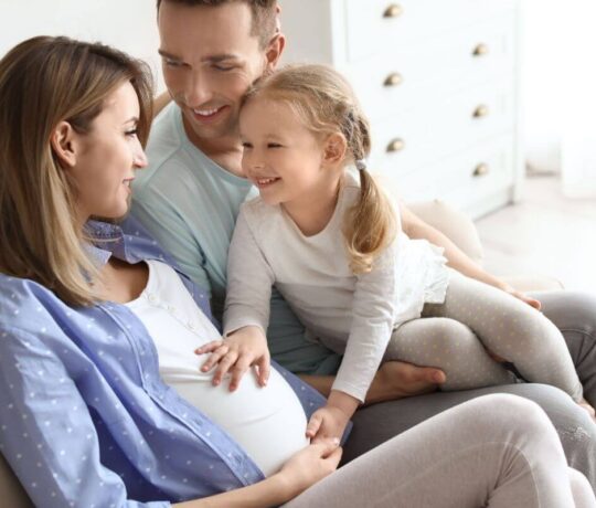 pregnant woman with a young girl touching her belly and a man smiling at her